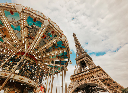Low angle view of Tour Eiffel and colorful carousel. The Eiffel Tower (French: tour Eiffel) is a wrought-iron lattice tower on the Champ de Mars in Paris, France, and its tallest structure. It is named after the engineer Gustave Eiffel, whose company designed and built the tower. Locally nicknamed \