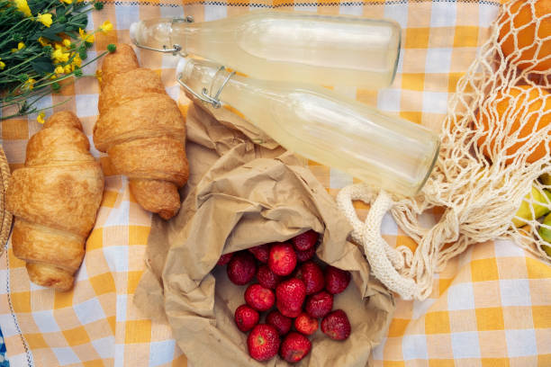 A small picnic with croissants, strawberries, and lemonade on an orange checkered blanket