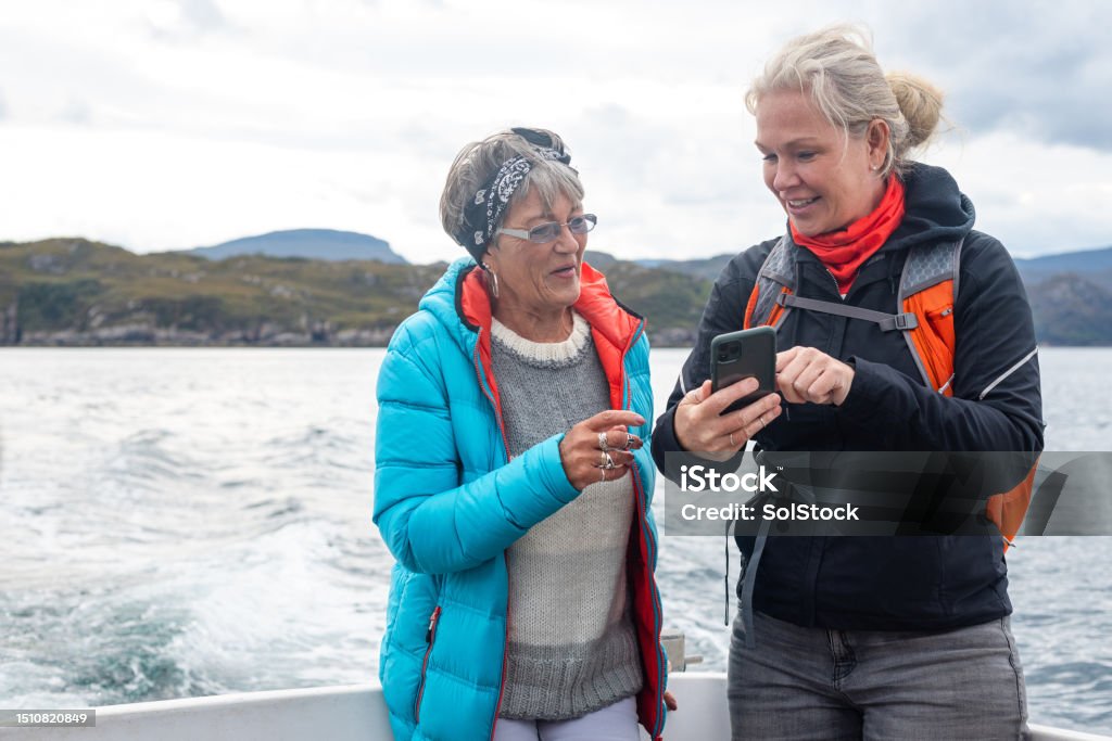 Quality Time With Mum A mother and daughter enjoying a weekend away together in Torridon, Scotland, they are on a tourboat, enjoying an excursion out at sea. One woman is showing her mother a picture she has taken on her phone while they both smile. Journey Stock Photo