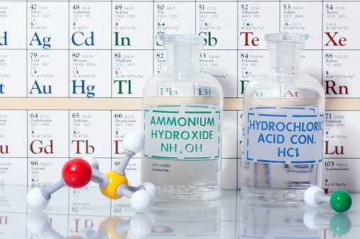 A closeup of two glass flasks of acid and base solutions with structures.