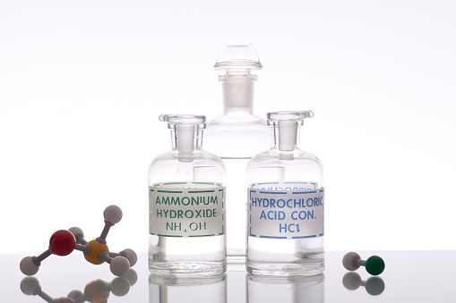 A closeup of glass flasks of acid and base solutions with structures isolated on a white backdrop.