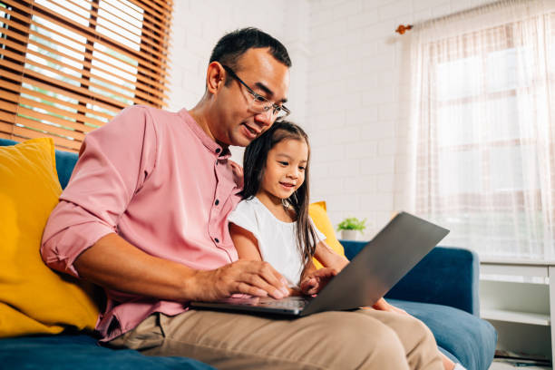 istock Father using laptop playing with daughter in living room 1510828323