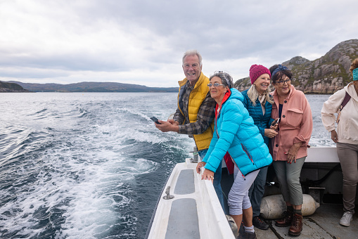 A group of friends enjoying a weekend away together in Torridon, Scotland, they are on a tourboat, enjoying an excursion out at sea. One woman is enjoying the breeze from the sea and another man is looking at the camera and smiling.