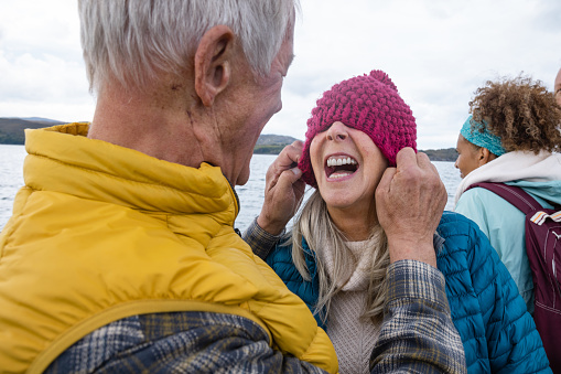 A mature couple enjoying a weekend away together in Torridon, Scotland, they are on a tourboat, enjoying an excursion out at sea. The man is pulling his wife's hat over her eyes while she laughs.