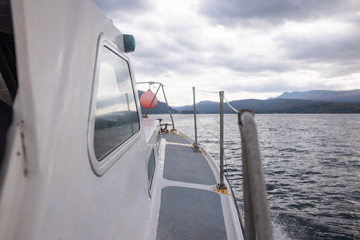 A tourboat out at sea in Torridon, Scotland. All that can be seen of the boat is part of the outside with the sea and mountain range surrounding it.