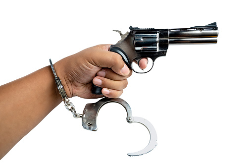 Arrested man with a handcuff on his hand holding a handgun isolated over white background
