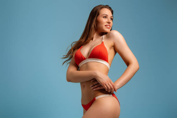 istock Happy young fit woman in bikini looking over shoulder while standing against blue background 1510853837