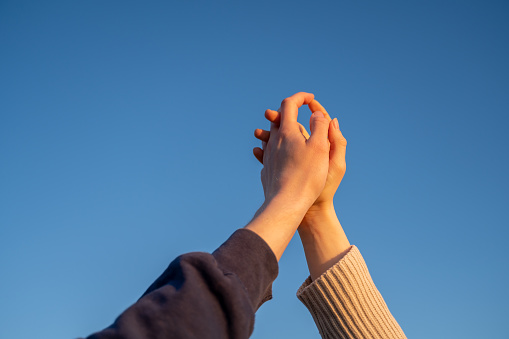Two persons holding hands against blue sky at sunset