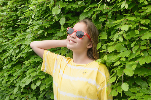 A teenage girl enjoy summer. Portrait, space for textin. Red sunglasses and a yellow shirt against a background of green foliage.