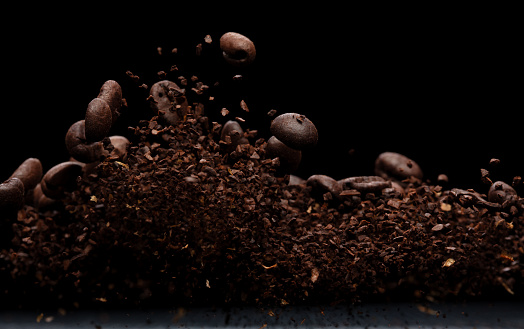Coffee powder fly explosion, Coffee crushed ground float pouring, wave like smoke smell. Coffee ground powder splash throwing in mid Air. Black background Isolated selective focus blur