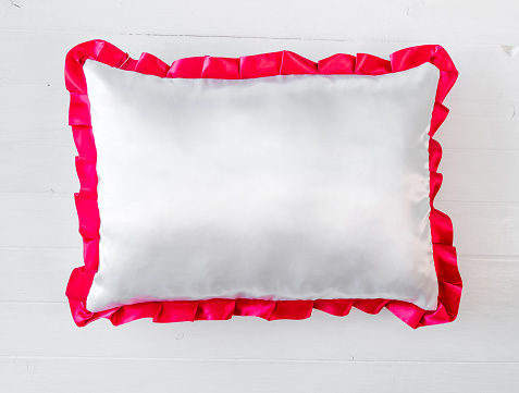 White pillow with pink frill on a white table