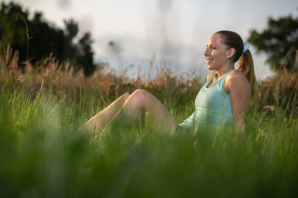A woman with a dog stopped after a run and checks the time on her sports watch with a sports app and phone. She ran through nature in the sunset, in the background wheat fields, green grass, trees and blue clear sky. Sunset. Copy space. He is looking towards the sunset. she reached her running goal