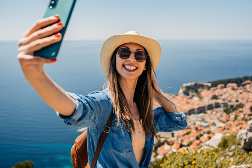 Young female tourist taking selfies from a high viewpoint above Dubrovnik in Croatia.