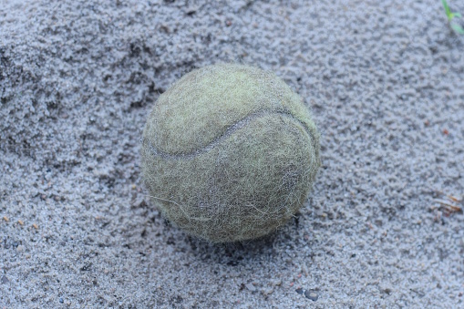 one old dirty yellow tennis ball lies on the gray sand in the street