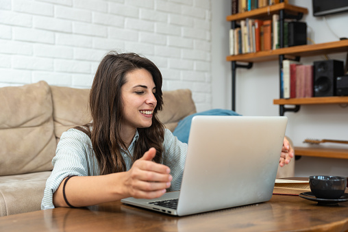 Young smart intelligent student woman sitting at home on floor working as freelancer distant foreign language professor, teaching people english on her laptop computer online from home via web camera