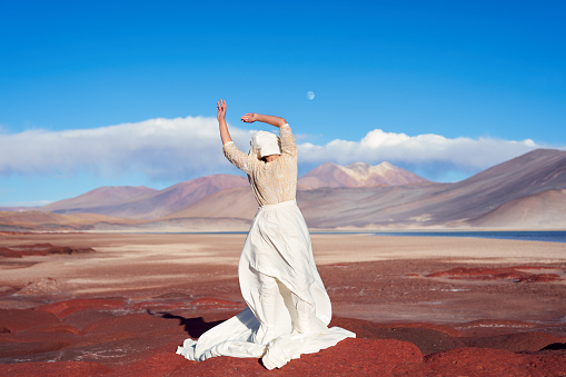 conceptual artistic portrait woman with long dress and face covered with cloth on red stones in Piedras Rojas San Pedro de Atacama