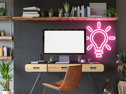 Industrial Style Cozy Workspace with an Empty Mockup Computer Screen and a Neon Light Bulb Sign. 3D Render