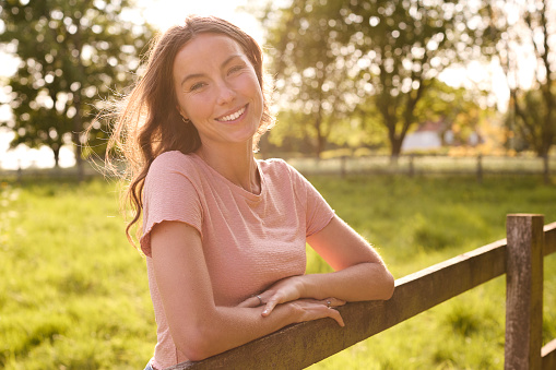 Portrait Of Smiling Woman Leaning On Fence On Walk In Countryside