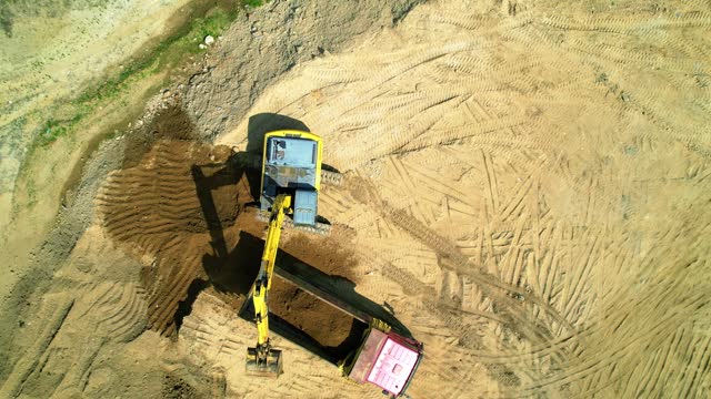 Aerial footage shows a construction site excavator loading sand into a truck
