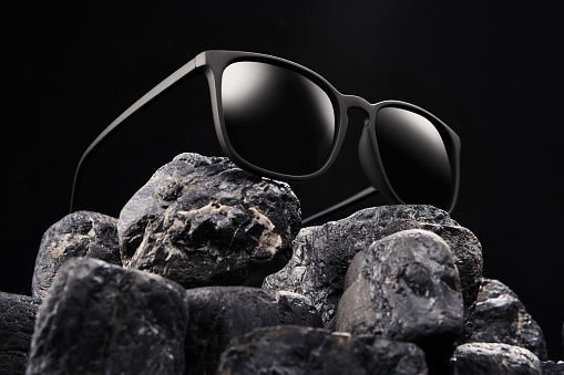 Open sunglasses, sun shades in plastic frame is on black stones on dark background. Bottom view. Blindness, loss of sight, eye disease, cecity, ablepsia, depression, doldrums, despondency concept.