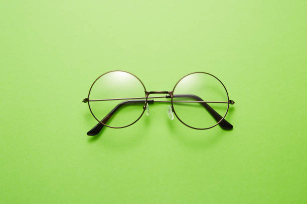 Glasses in round thin metal frame isolated on green surface. Top view. Folded unisex eyeglasses is in center. Clear vision. Place for text. Studio shoot still life. Specs, eyewear, modern accessory.