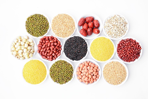 A variety of raw cereals of different colors and types presented in small bowls against a white background