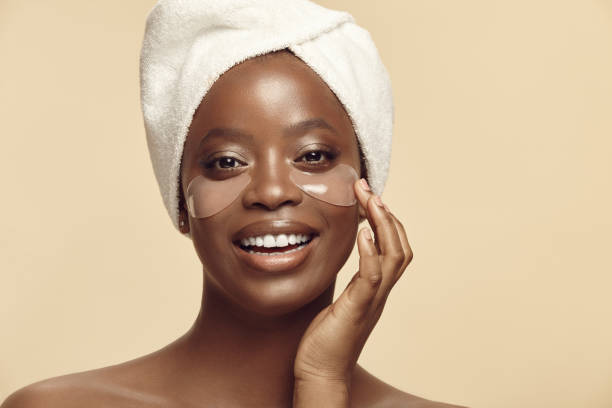 istock Attractive young African woman applying beauty eye patch and cheerful smiling while standing against beige background with a free copy space 1511168280