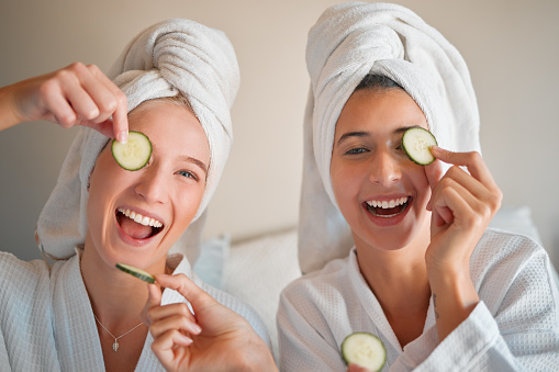 Friends, cucumber and teenager, girl and facial, happy with pampering and beauty in portrait with skincare treatment. Happiness, people have fun together and female friendship, cosmetics and laughter