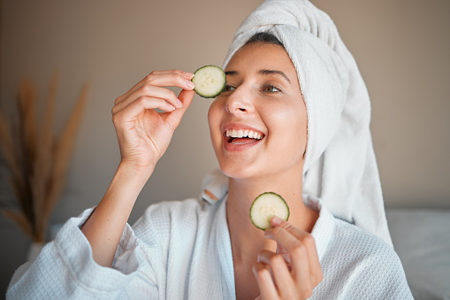 Happy woman, cucumber and natural skincare for beauty, cosmetics or facial treatment at spa. Female smiling and applying vegetable to eyes for organic healthcare, hydration or dermatology at salon