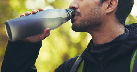 Man, hiking or drinking water in nature forest, woods or fitness environment for break, electrolytes or healthcare wellness. Hiker, backpacker or sports bottle for rest, recovery or thirsty workout