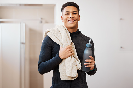 Portrait, black man and bottle in locker room of gym for rest, cleaning towel and shower after exercise. Happy sports guy, athlete and break after workout, training and wellness in fitness bathroom
