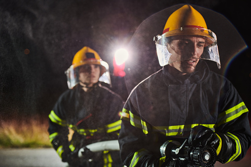 Firefighters using a water hose to eliminate a fire hazard. Team of female and male firemen in dangerous rescue mission