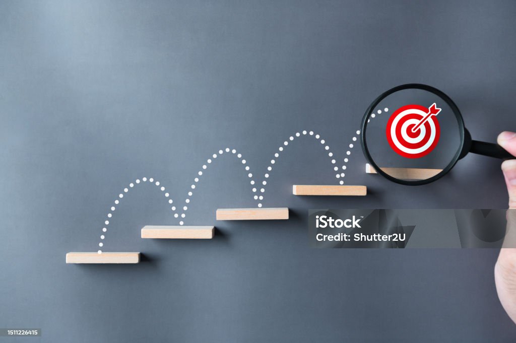 Unlock potential of business success stairs dart and dartboard targets magnifying glass with hand on gray background. Explore opportunities growth embrace steps to achieve ambitions and goal concept. Aspirations Stock Photo