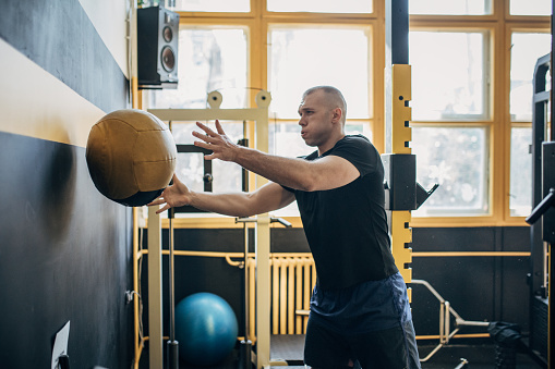 One man, fit male exercising with medicine ball in gym.