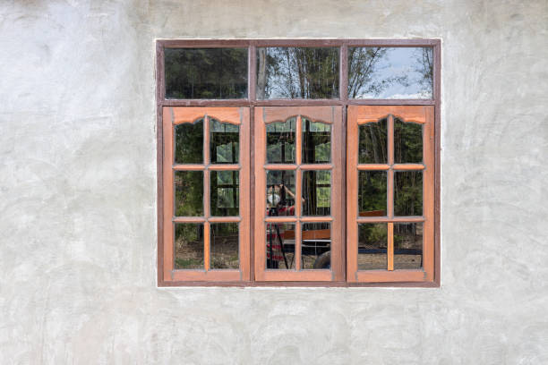 A gray concrete wall background decorates an old wooden glass window of a house with bamboo groves in the Thai countryside in reflected light.