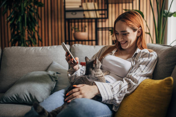 Young woman cuddling with cat at home ad using smartphone