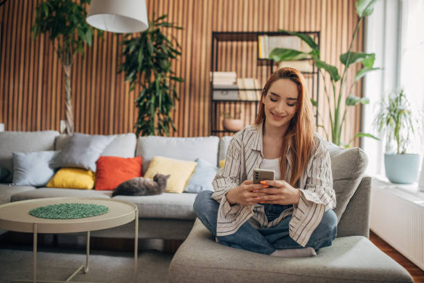 Beautiful woman sitting on the sofa and using smart phone stock photo