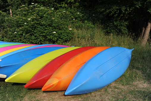 Colorful kayaks stacked in a row on a green meadow on a sunny summer day in Poland