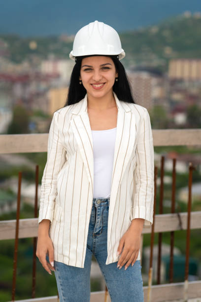 istock Smiling young female architect in a hard hat on a construction site, looking at the camera. Construction manager, manager, engineer at the construction site. Vertical photo 1511286876