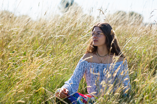 Woman sitting looking away from the camera in a wheat field practising mindfulness while on vacation in Toulouse, South of France.