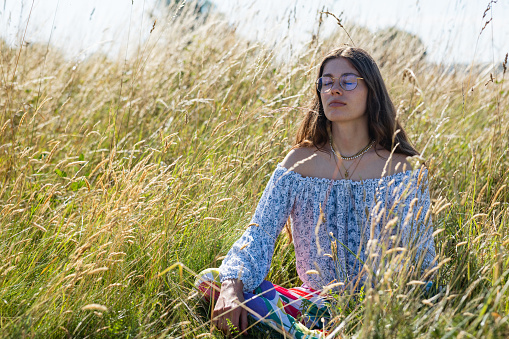 Woman sitting with her eyes closed in a wheat field practising mindfulness while on vacation in Toulouse, South of France.