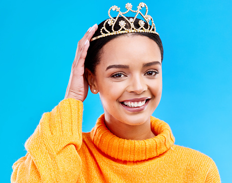 Pride, crown and portrait of woman in studio for celebration, princess and party. Smile, beauty and fashion with female and tiara on blue background excited for achievement, winner and prom event