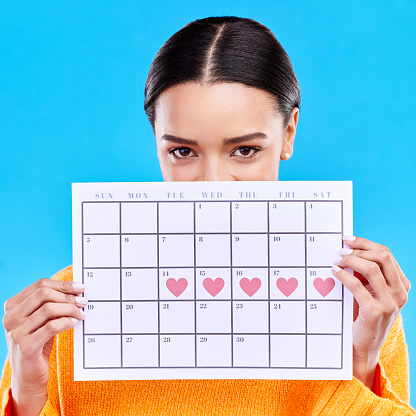 Calendar, heart and woman on blue background for period schedule, planning and menstruation in studio. Time management, strategy and eyes of girl with month poster for date, weekly planner and cycle