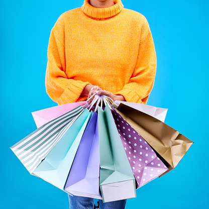 Woman, hands and shopping bags for purchase, sale or luxury accessories against a blue studio background. Hand of female shopper holding gift bag, buy or discount presents of retail products or items