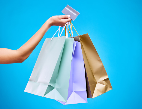 Woman, hands and shopping bags with credit card for purchase, sale or discount against a blue studio background. Hand of female shopper holding gift bag or presents for banking transaction or buying