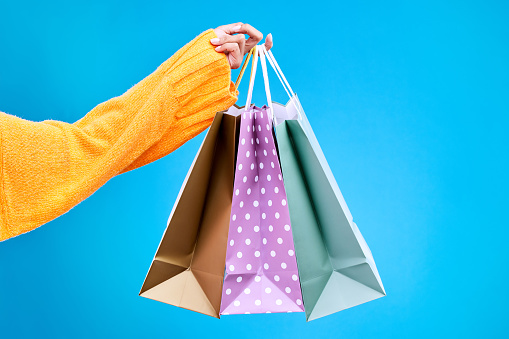 Woman, hands and shopping bags in studio of purchase, luxury accessories or sale against a blue background. Hand of female shopper holding gift bag, buy or presents of retail products on mockup