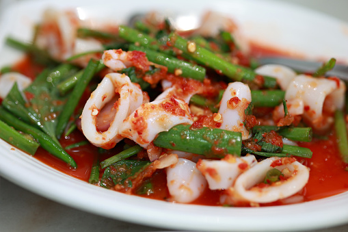 Thai squid chili salad with spices and herbs served on a white plate close up