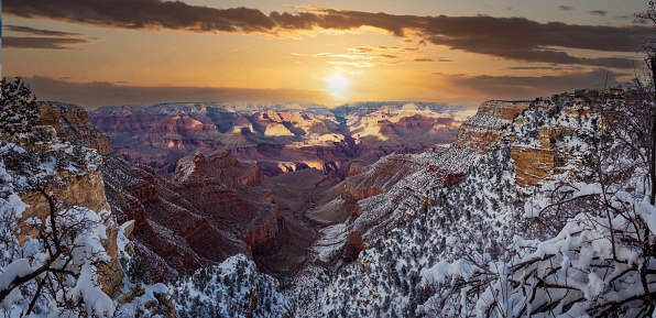 The Grand Canyon framed by the snow cover rim in the foreground and the white clouds with blue skies in the distance.