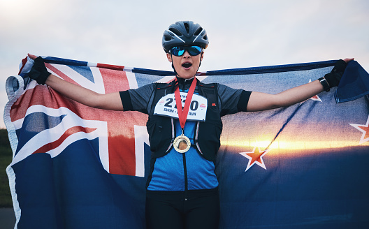 Winner sports, happy woman from New Zealand with flag and gold medal winning outdoor cycling race or triathlon. Happiness, win and cyclist with smile, fitness and world record with national pride.