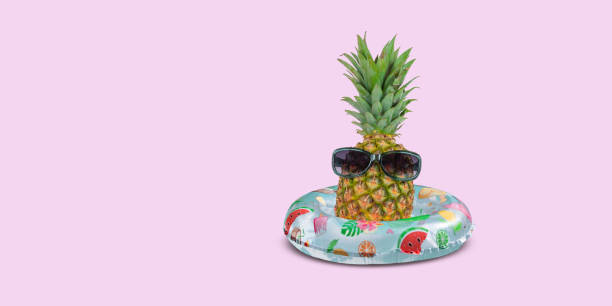 istock Pineapple with sunglasses in inflatable swim ring on pink background. 1511333950
